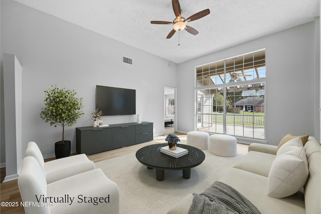 living room featuring hardwood / wood-style flooring, ceiling fan, and a textured ceiling