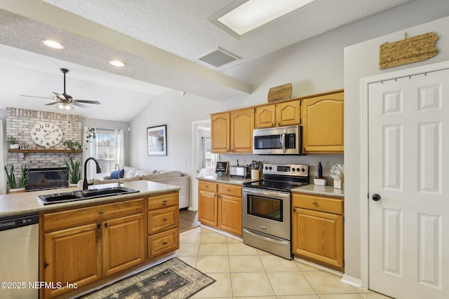 kitchen with lofted ceiling, sink, light tile patterned floors, stainless steel appliances, and a fireplace