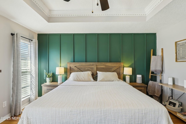 bedroom featuring ceiling fan, a tray ceiling, and a textured ceiling