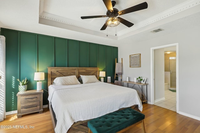 bedroom with connected bathroom, a tray ceiling, ceiling fan, and light wood-type flooring