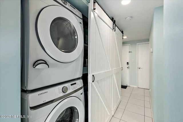 laundry area with light tile patterned flooring, a barn door, and stacked washer / drying machine