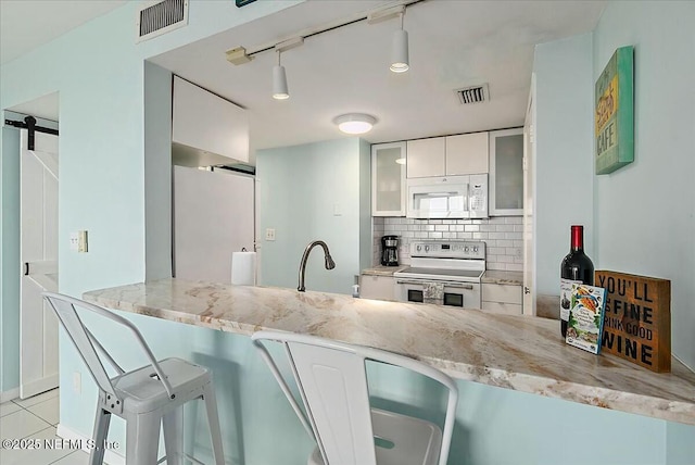 kitchen featuring white cabinetry, light stone counters, white appliances, a barn door, and backsplash