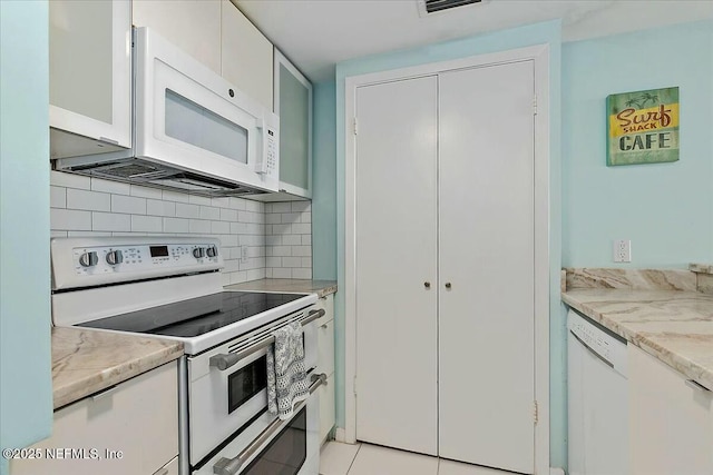 kitchen with backsplash, white appliances, light tile patterned floors, and white cabinets