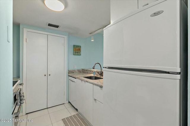 interior space featuring sink, white appliances, light tile patterned floors, white cabinetry, and light stone counters