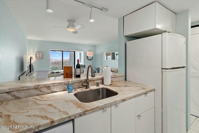 kitchen with sink, white cabinetry, white refrigerator, ceiling fan, and light stone countertops