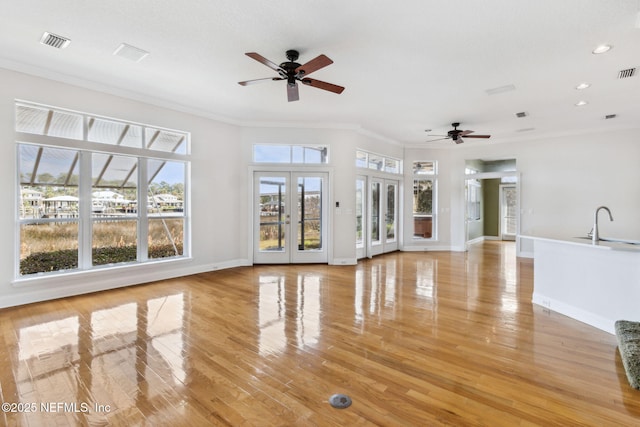 unfurnished living room with sink, crown molding, ceiling fan, light hardwood / wood-style floors, and french doors