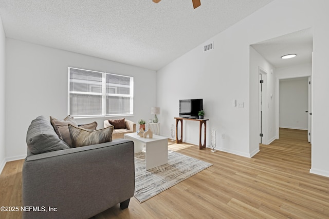 living room with lofted ceiling, ceiling fan, light hardwood / wood-style flooring, and a textured ceiling