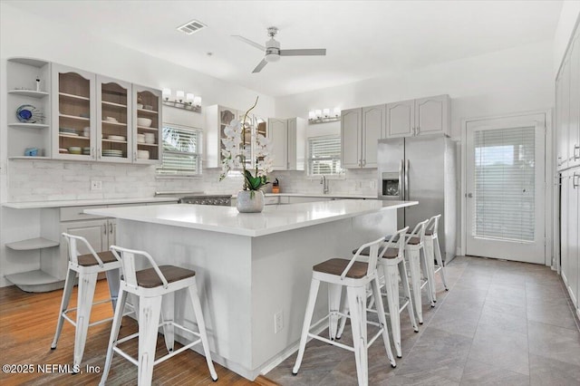 kitchen featuring ceiling fan, backsplash, a kitchen breakfast bar, a center island, and stainless steel refrigerator with ice dispenser