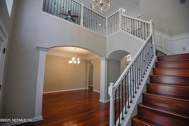 stairs featuring wood-type flooring, ornamental molding, an inviting chandelier, and a towering ceiling