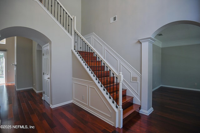 staircase with a high ceiling, ornamental molding, hardwood / wood-style floors, and decorative columns