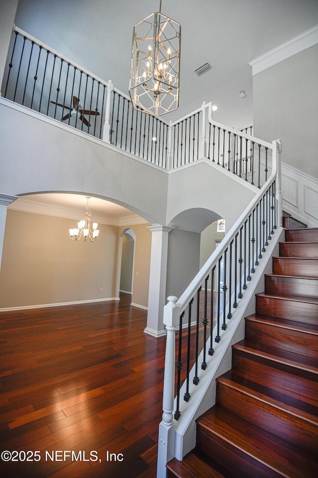 staircase with an inviting chandelier, a towering ceiling, ornamental molding, and wood-type flooring