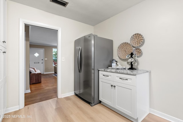 kitchen with stainless steel fridge, light stone countertops, light hardwood / wood-style floors, and white cabinets