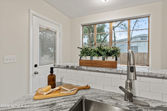 interior space featuring light stone counters, sink, and backsplash