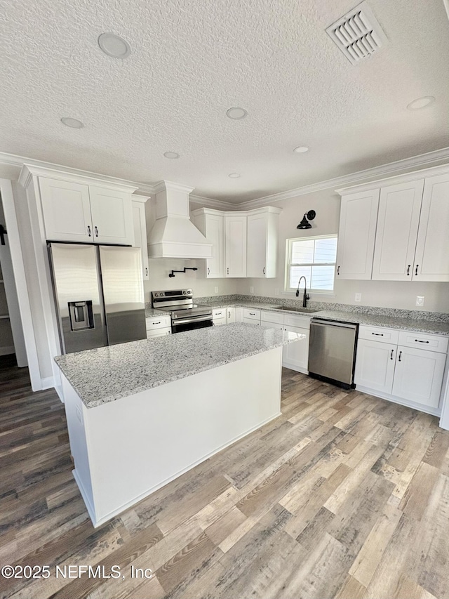 kitchen featuring visible vents, appliances with stainless steel finishes, wood finished floors, custom exhaust hood, and white cabinets