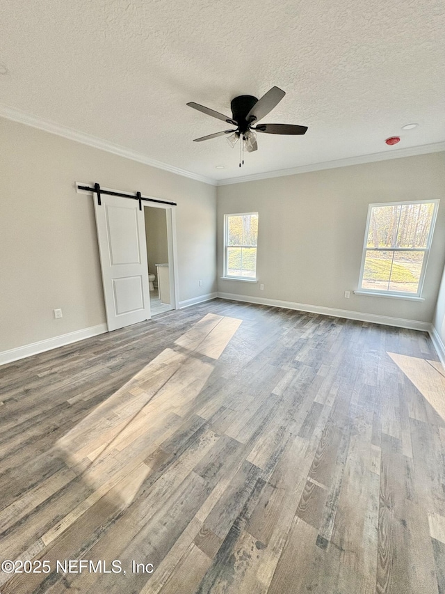 unfurnished bedroom with crown molding, baseboards, a barn door, wood finished floors, and a textured ceiling