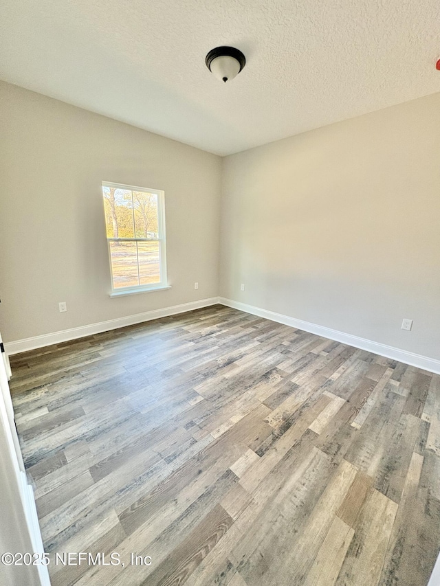 spare room with wood finished floors, baseboards, and a textured ceiling