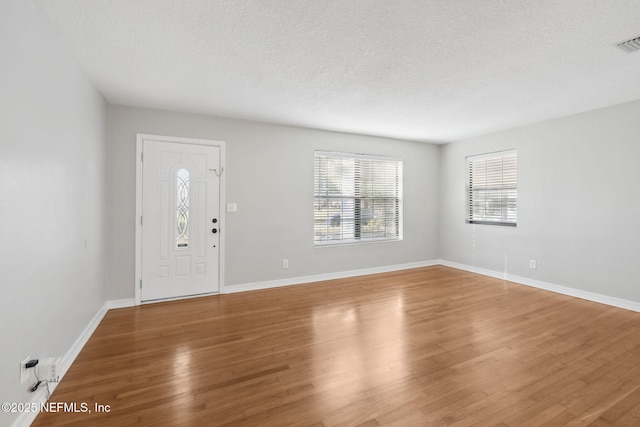 foyer with visible vents, a textured ceiling, baseboards, and wood finished floors