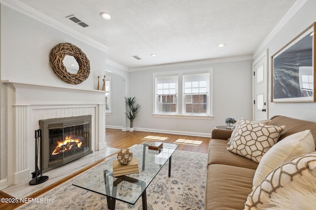 living room with a fireplace, wood finished floors, visible vents, baseboards, and ornamental molding