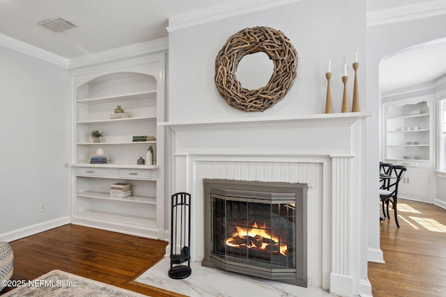 room details with built in features, a brick fireplace, crown molding, and wood finished floors