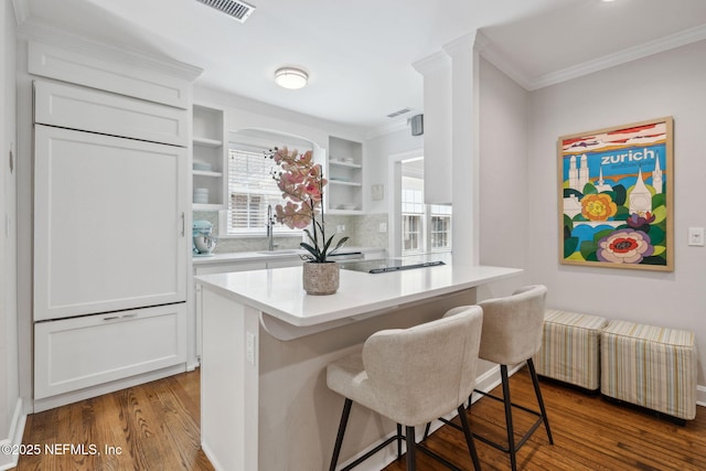 kitchen with dark wood-style flooring, crown molding, light countertops, white cabinets, and a kitchen bar