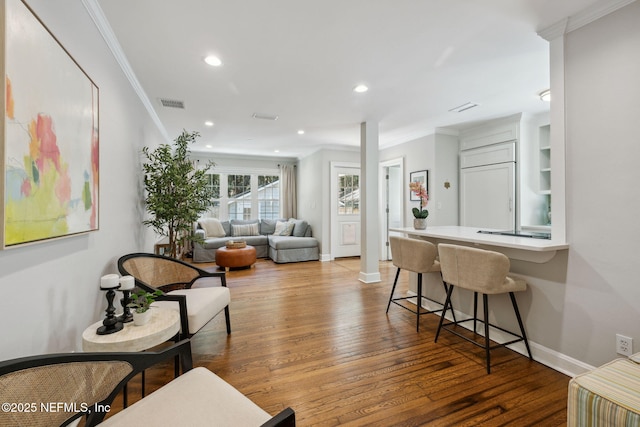 living room featuring hardwood / wood-style flooring, crown molding, visible vents, baseboards, and ornate columns