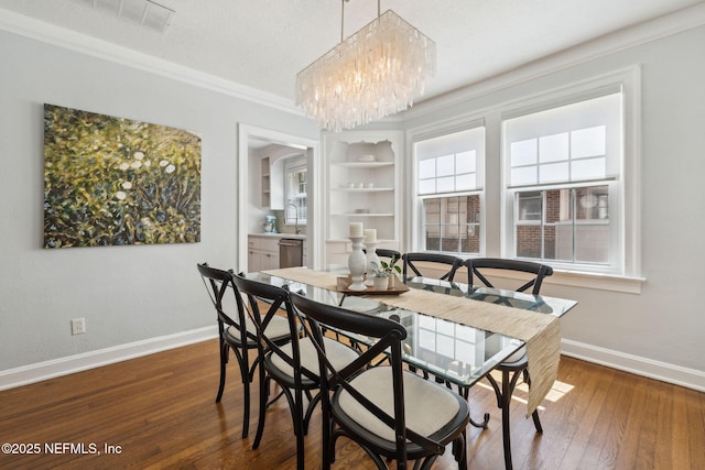 dining room with baseboards, built in features, wood-type flooring, ornamental molding, and a chandelier