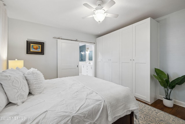 bedroom with ceiling fan, a barn door, wood finished floors, baseboards, and ensuite bath