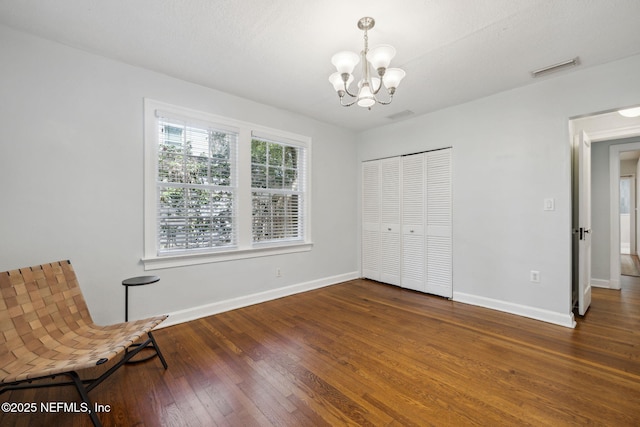 unfurnished room featuring baseboards, visible vents, an inviting chandelier, and hardwood / wood-style flooring