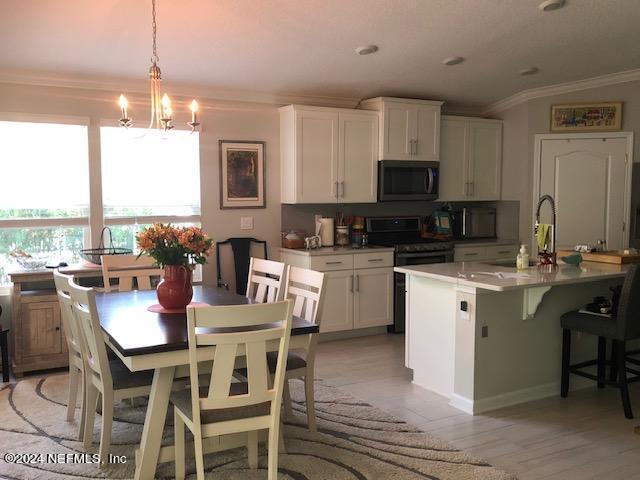 kitchen featuring sink, range with electric stovetop, white cabinets, a center island with sink, and decorative light fixtures