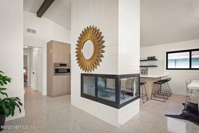 living room featuring a tiled fireplace, beam ceiling, and high vaulted ceiling