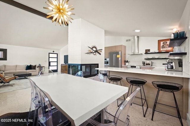 kitchen featuring wall chimney exhaust hood, appliances with stainless steel finishes, a kitchen breakfast bar, kitchen peninsula, and decorative backsplash