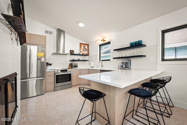 kitchen with lofted ceiling, a kitchen bar, kitchen peninsula, stainless steel appliances, and wall chimney range hood