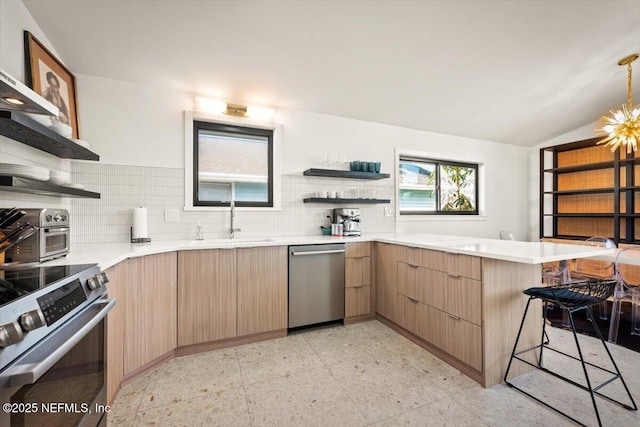 kitchen with appliances with stainless steel finishes, decorative light fixtures, sink, a kitchen bar, and kitchen peninsula