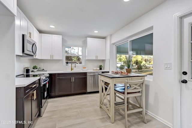 kitchen with sink, a breakfast bar area, appliances with stainless steel finishes, white cabinetry, and dark brown cabinets