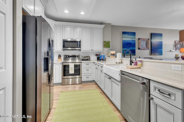 kitchen featuring sink, light hardwood / wood-style flooring, white cabinetry, stainless steel appliances, and kitchen peninsula