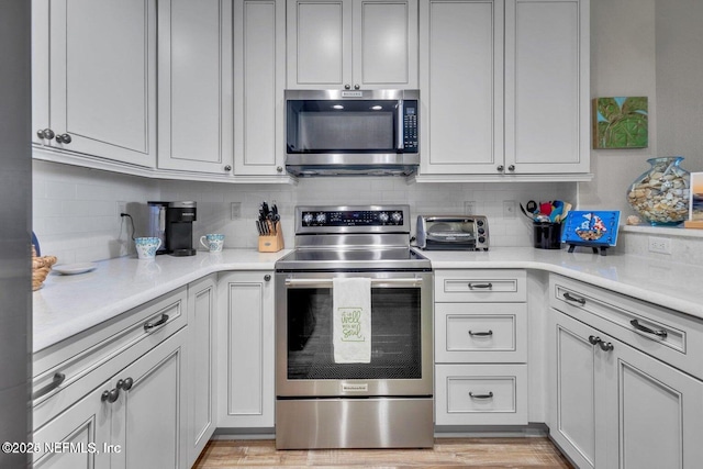 kitchen featuring tasteful backsplash, appliances with stainless steel finishes, light hardwood / wood-style flooring, and white cabinets