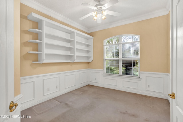 carpeted empty room with a wainscoted wall, ceiling fan, and ornamental molding