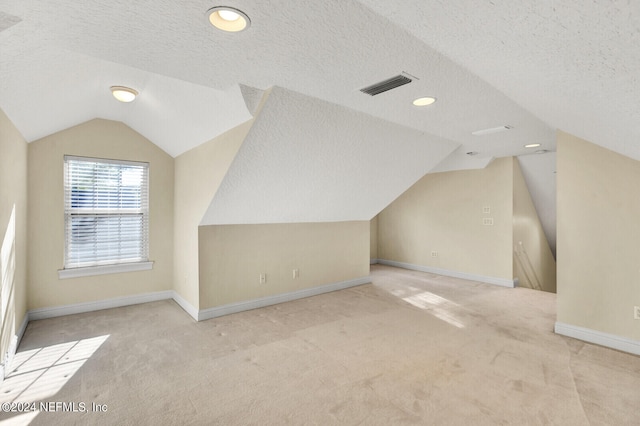 bonus room featuring lofted ceiling, a textured ceiling, carpet flooring, and visible vents