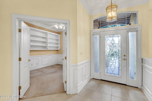 carpeted foyer entrance featuring tile patterned flooring, wainscoting, a decorative wall, and an inviting chandelier