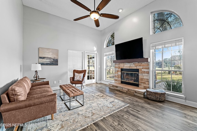 living room with ceiling fan, a towering ceiling, a fireplace, and hardwood / wood-style floors