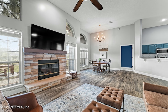 living room with ceiling fan with notable chandelier, hardwood / wood-style floors, a fireplace, high vaulted ceiling, and a textured ceiling