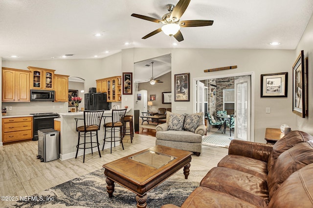 living room with a textured ceiling, vaulted ceiling, ceiling fan, and light wood-type flooring