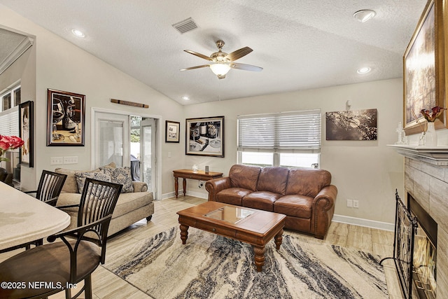 living room with a healthy amount of sunlight, vaulted ceiling, a tile fireplace, and light wood-type flooring