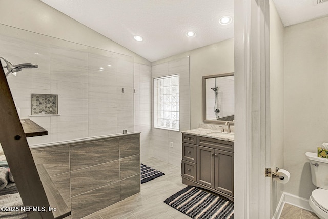 bathroom with vaulted ceiling, a tile shower, vanity, and toilet