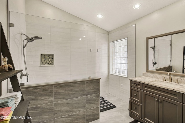 bathroom with lofted ceiling, vanity, and a tile shower