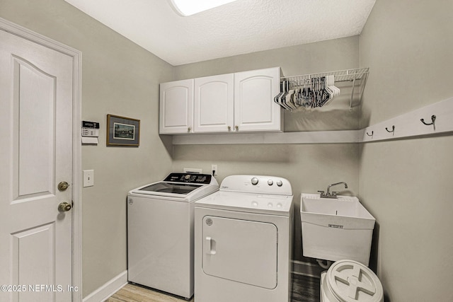 clothes washing area featuring cabinets, sink, washing machine and dryer, and light hardwood / wood-style flooring