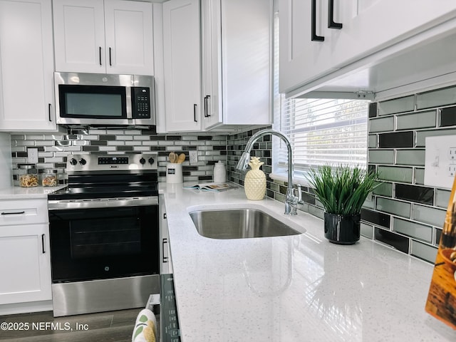 kitchen with tasteful backsplash, white cabinetry, sink, stainless steel appliances, and light stone countertops