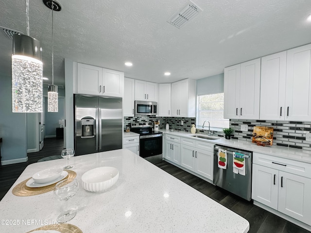 kitchen with pendant lighting, sink, appliances with stainless steel finishes, light stone counters, and white cabinets