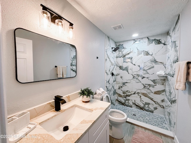 bathroom with vanity, a textured ceiling, toilet, and tiled shower