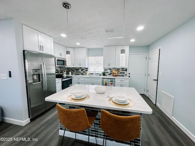 kitchen with stainless steel appliances, a center island, decorative backsplash, white cabinets, and decorative light fixtures